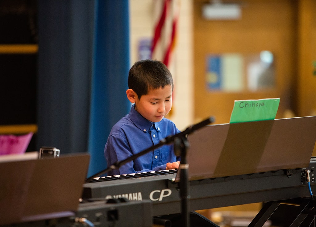 a young boy watches his hands while playing the keyboard