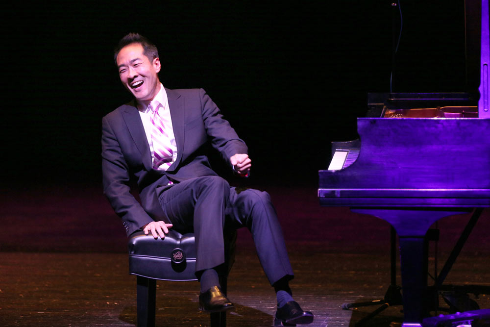 Alpin Hong sitting on stage, laughing