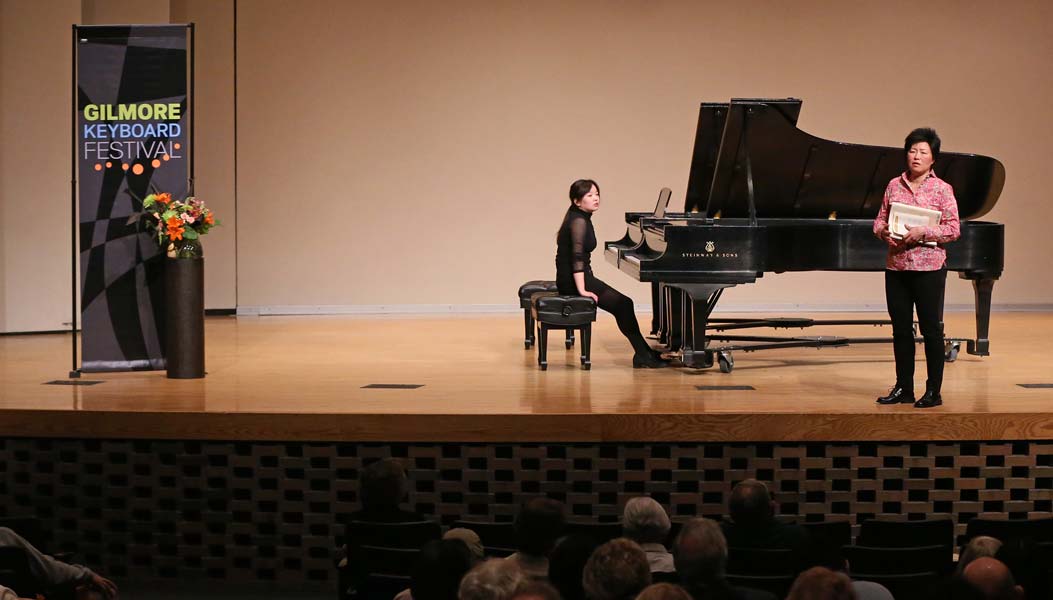 Katherine Chi standing on stage with a student in front of an audience