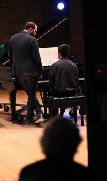 Kirill Gerstein standing while talking to a student at the piano