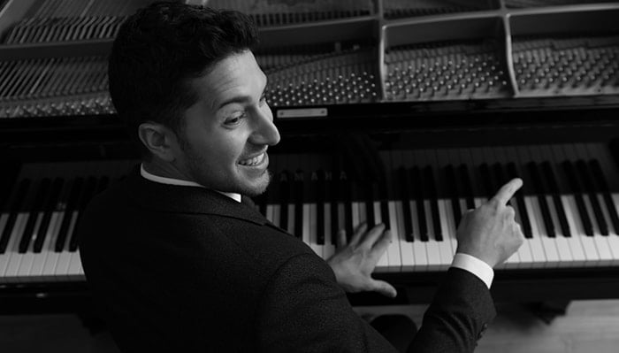 emmet cohen smiles and turns while playing the piano