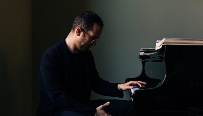 igor levit plays the piano in dramatic lighting