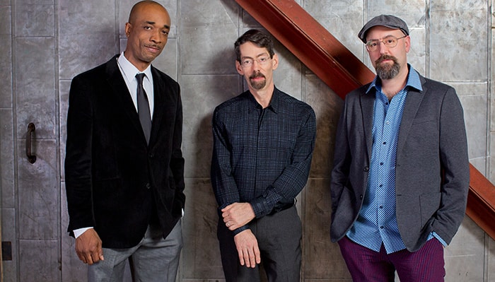 the Fred Hersch Trio poses for a portrait against a gray wall