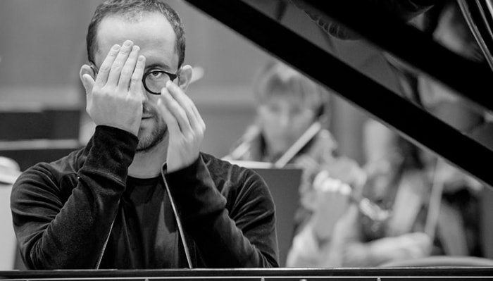 Igor levit sits behind a piano and covers one eye with his hand