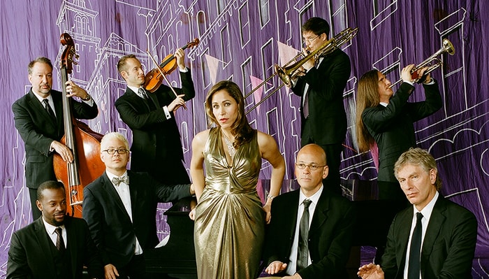 Members of pink martini pose for a portrait in front of a purple backdrop