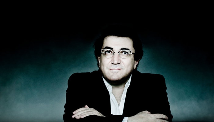 Sergei Babayan sits in front of a dark background with a blue light and looks up for a portrait