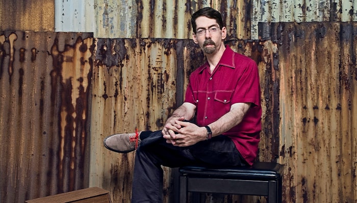 fred hersch poses for a portrait in front of an industrial wall