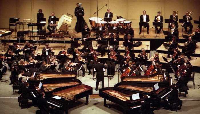 image of musicians performing six pianos