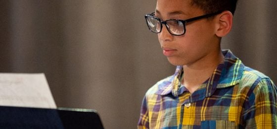 a boy looks at sheet music while playing the piano